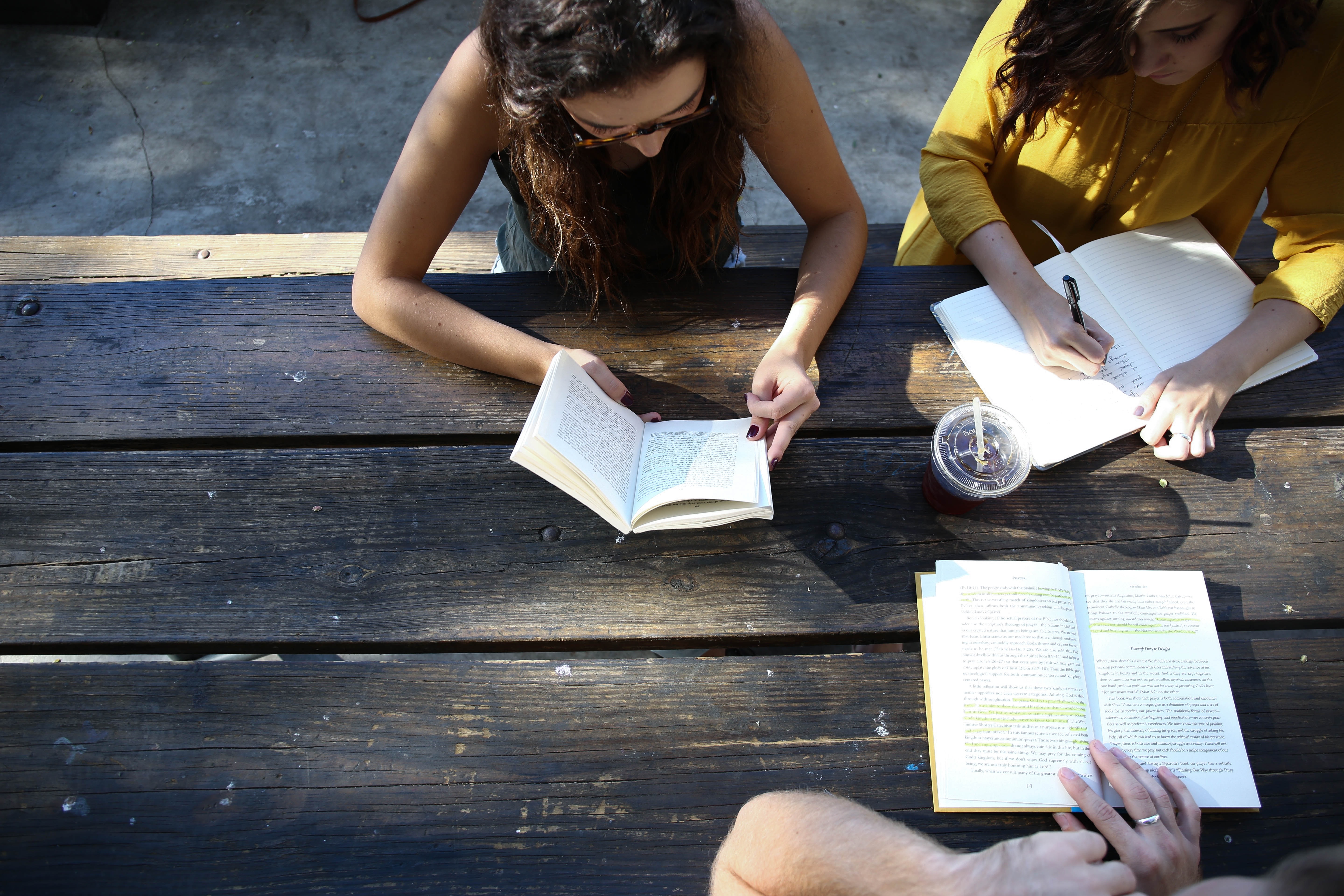 Three people sit at a table with open books, appearing to discuss the content.