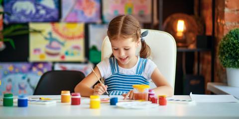 Small child paints with paintbrush at a table.