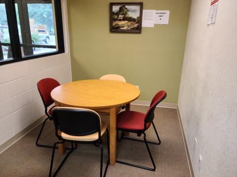 Round table surrounded by four chairs in a small room with a window looking outside.