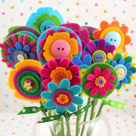 Colorful felt flowers made from felt and buttons in a clear vase.